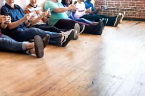 A group of people sitting on a pre-finished hardwood floor playing games on their mobile phones.