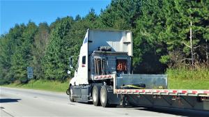 A semi-truck is driving on I75 in Ohio and there is a sign that says the speed limit is 65 miles per hour.