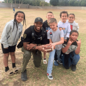 A Surprise PD police officer poses with joyful children in a vibrant field.