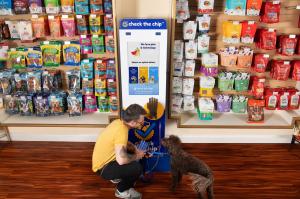 Good Samaritan kneels next to lost curly brown dog, scanning for a microchip