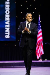 Jairek Robbins on stage smiling in Toronto with American flag behind him in Toronto.