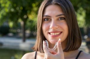 A beautiful, smiling Turkish woman happily holding an Invisalign aligner, showcasing her satisfaction with the results.