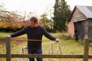 A man in a black long-sleeved shirt carefully measures a garden fence for repair