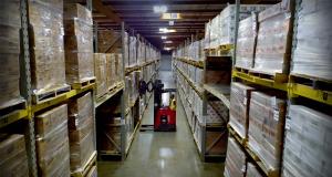 A picture of stacked goods in a warehouse with a forklift in the middle