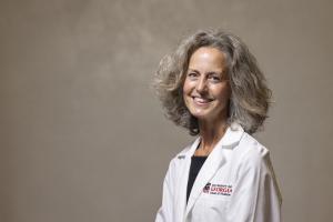 Dr. Erica Brownfield sits against a backdrop wearing a UGA School of Medicine lab coat