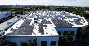 A two-story commercial building with a solar system on the roof. The solar panel arrays are in various shapes due to roof obstacles such as air conditioning units.
