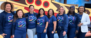 A group of women wearing blue shirts stands together in front of a boat, smiling.