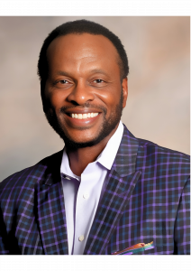 A smiling Black man wearing a stylish plaid suit, exuding confidence and charm in a vibrant setting.