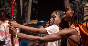 Female instructor showing a young female student how to hold a bow during archery.