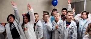 A diverse group of children dressed in white lab coats.