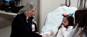 A hospital staff assists a young girl in a hospital bed.