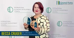 Becca Cruger EDC Director of Workforce Development stands in front of an IEDC step and repeat holding a bronze and silver award.