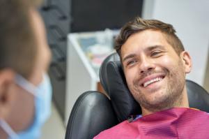 Male patient in an exam chair next to a male dentist in a face mask.