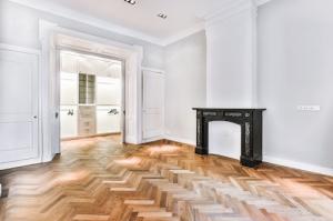 A newly built, elegant room featuring a fireplace and hardwood flooring in a striking herringbone pattern.