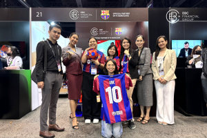 يلتقط أعضاء فريق EBC Financial Group والحضور صورة معًا في معرض iFX Expo Asia 2024 في بانكوك، حيث يعرضون بضائع تحمل العلامة التجارية المشتركة لنادي FC Barcelona.