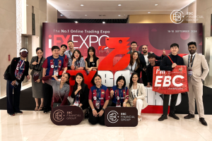 A group photo of EBC Financial Group team members at the iFX Expo Asia 2024 in Bangkok, standing in front of the large red iFX Expo logo