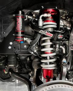 This image shows a close-up of a high-performance suspension upgrade installed on a vehicle. The suspension features a prominently displayed red coilover shock absorber branded "RIDE Shocks" with a remote reservoir. The shock is equipped with silver coils