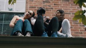 Mr. FoW and two women sit on the rooftop of a house, gazing intently at the camera, with a brick wall in the background.