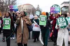 A photograph of a group of women walking together in a road, holding signs saying "ERA Now" in support on the Equal Rights Amendment