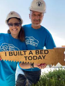 Two Lowe’s Independent Service Providers wear white safety hats and blue Lowe's Services Serves t-shirt at a Bunks Across America bed build.