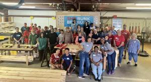 A volunteer group photo inside a bed building shop with lumber and power tools.