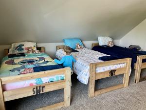 A child stands next to one of three newly built, delivered and assembled SHP beds made up with cozy bedding and Jockey Being Family blankets and teddy bears.