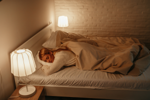 Young woman sleeping in her bed with the room lights on