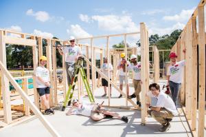 The City Detect team pose around various areas of a recently framed home during a volunteer construction day. The team is wearing their City Detect Cleanup Crew team shirt.