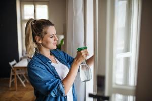 A woman cleans a window using a spray bottle filled with an eco-friendly cleaning solution. This represents the growing trend toward non-toxic home products and chemical-free wellness products. Sisel offers a range of organic household essentials designed