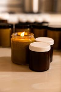 a jar of topical salve, unlabeled, with a wick sunk into it is burning like a candle with other jars of salve (with lids) around it, all unlabeled