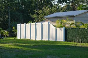 A white vinyl privacy fence enclosing the backyard of a simple beige country home surrounded by a lush, vibrant green garden.