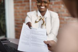 black woman wearing an off-white jacket receiving resume from a potential applicant