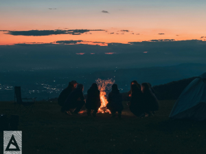 Group of people around a bonfire overlooking city at night