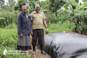 Two farmers in Kenya standing beside a Sistema.bio biodigester, showcasing sustainable farming practices and renewable energy solutions.