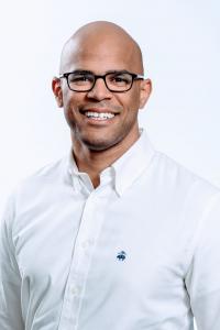 alt= Dr. Ramon Lizardo, CEO of Tele911,  is wearing glasses, a white collared shirt and smiling against a plain background.