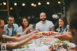 a group of people holding plates of food at a dinner party under string lights