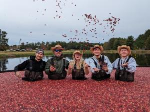 five people waste deep in a cranberry bog with cranberries in the air