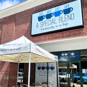 The exterior of 'A Special Blend' coffee shop features a large sign with the slogan 'Community in a Cup' above the entrance and a branded canopy outside.