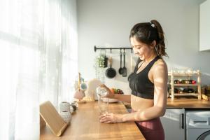 Young woman in athletic wear pouring water into a glass in a sunlit kitchen, representing a commitment to health and wellness. The image echoes Sisel International's mission to provide safe, toxin-free wellness products, honoring the pioneering vision of 