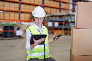 A female warehouse worker using a tablet to input data from a handheld inventory scanner into a mobile form.