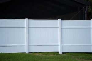 A white vinyl picket fence surrounding a green, well-maintained lawn, providing a secure boundary around the property’s backyard area.