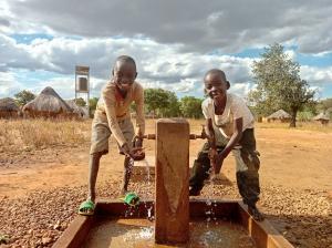 Two young children at a new tap in a village in an arid environment, with solar powered water tower in background