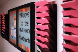 Blue "Welcome to the Heartwood Apartments" sign greets new residents surounded by red file folders