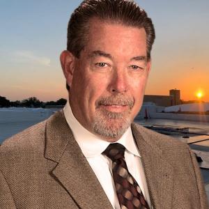 Bryan Davis, with a background in education leadership, pictured at sunset over a commercial roofing site, emphasizing his role in advancing Coryell Roofing's educational sector projects.