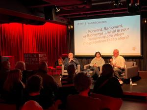 Ingo Günther, Lubna Hayatleh-Heinke, and Gordian Overschmidt seated on stage at Berlin Science Week, discussing decision-making in the context of migration, art, and societal impact.