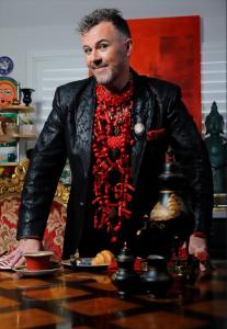 Man standing wearing a black jacket with massive red coral necklace