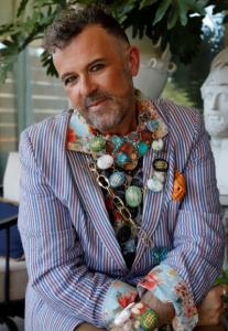 Man wearing a striped jacket wearing a layered collection of colorful cameos by Sugar Gay isber