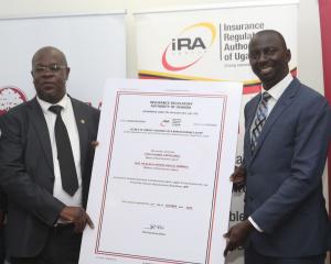 Benerd Obel, Director for Supervision, Insurance Regulatory Authority of Uganda and FINCA Uganda Managing Director- James Onyutta are standing together, holding a poster-sized version of the bancassurance license granted to FINCA Uganda.