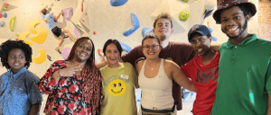 Group of people in front of a climbing wall, some posing with arms around each other.