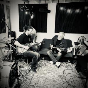 Parker Grones and Karl Mattson of Tough Ship are shown sitting across from each other in a recording studio rehearsing guitar parts.